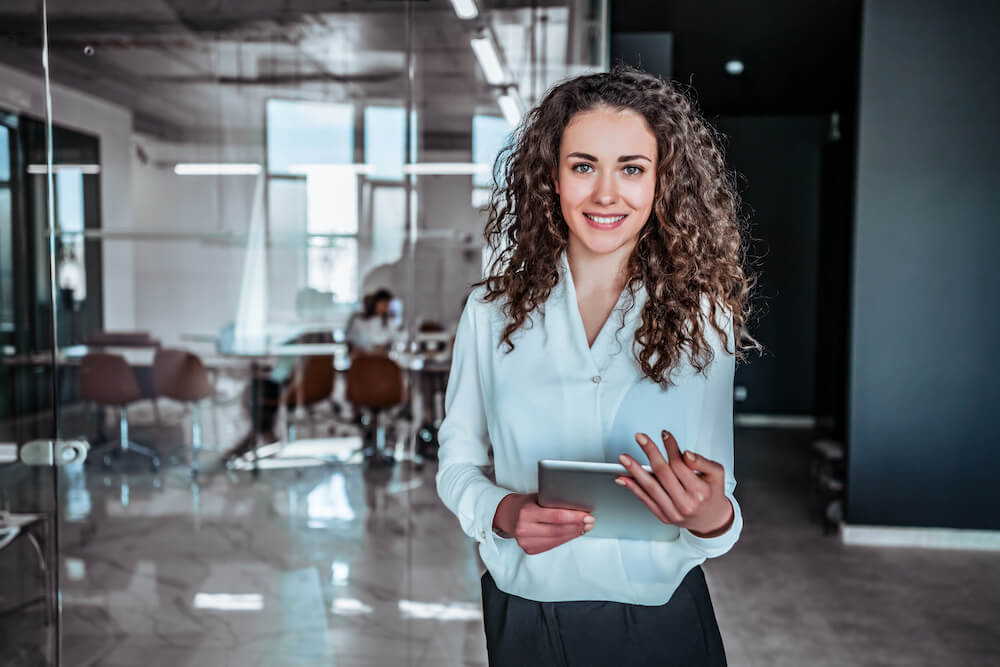 lady holding tablet and smiling in an office space while looking directly at the camera